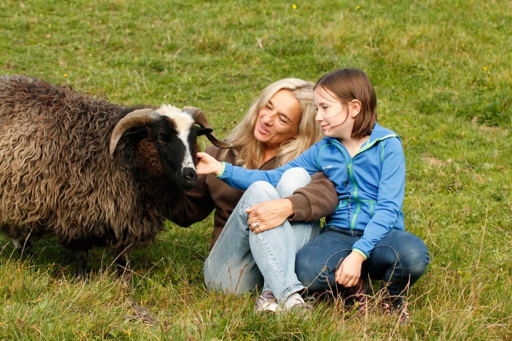 Frau und Mädchen streicheln Ziegenbock