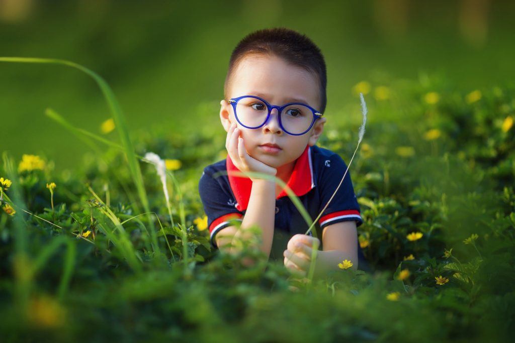 Kleiner Junge mit blauer Brille liegt in der Wiese